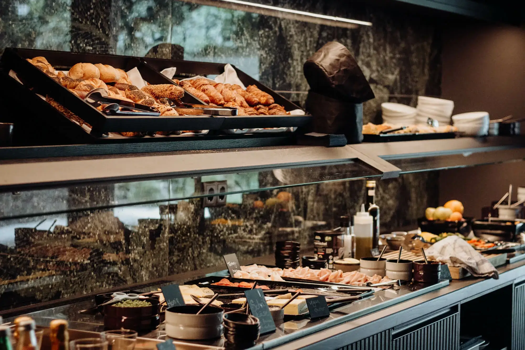 A large breakfast buffet with fresh products, including bread, pastries, cold cuts, cheese, fruit, cereal, and various beverages.